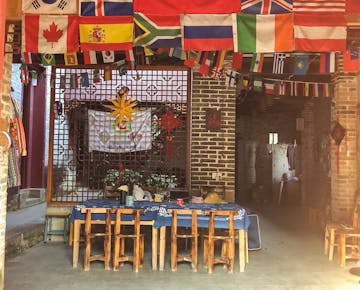 A cozy communal dining area with wooden tables and chairs, decorated with international flags hanging from the ceiling in a traditional brick building.