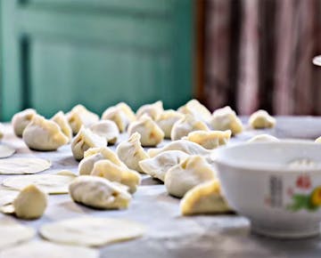 Homemade dumplings being prepared, with rows of raw dumplings and flat dough circles laid out on a floured surface, ready for cooking.