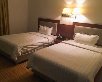 A hotel-style room with two double beds, crisp white bedding, and a wall lamp above a shared nightstand.