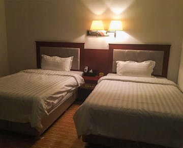 Another view of a cozy hotel room with two beds and a wall lamp, creating a warm and inviting atmosphere.