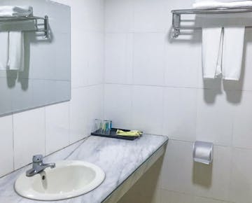 A bathroom with a marble sink countertop, mirror, towel rack, and basic amenities, all in a white-tiled setting.