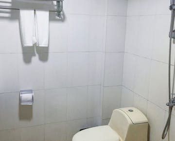 A clean, tiled bathroom with a toilet, handheld shower, towel rack, and toilet paper holder.
