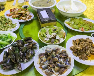 A large round table set with a variety of Chinese dishes including seafood, vegetables, and rice, ready for a group meal.