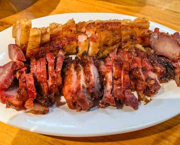 A plate of sliced crispy roast pork and barbecue pork, arranged neatly on a white plate.
