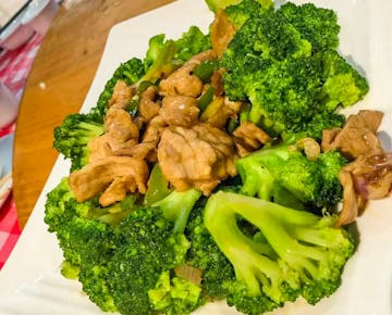 A plate of stir-fried pork and broccoli in a savory sauce, served on a white square plate.