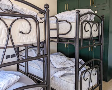 A shared bedroom setup with two sturdy black metal bunk beds and white bedding, situated next to green lockers with numbered doors.
