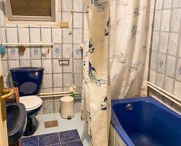 A tiled bathroom with a blue toilet, sink, and bathtub, complete with a curtain, shower.