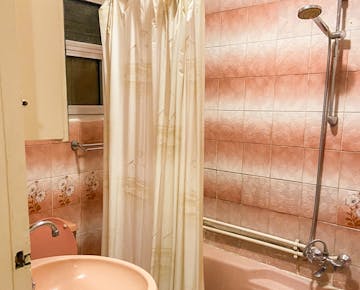A cozy bathroom with floral pink tiles, a peach-colored sink, a shower with a handheld head, and a curtain over a pink bathtub.