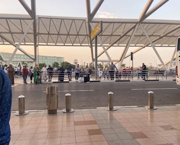 Families and travelers wait near the curbside pickup zone outside Cairo International Airport under a modern canopy structure, ready to greet new arrivals.