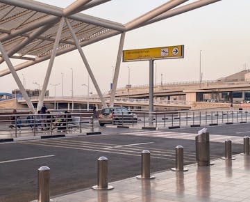 Outside the international arrivals terminal at Cairo International Airport, with people waiting by the curb beneath a modern metal canopy.