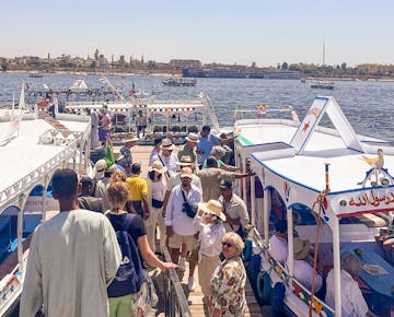 A busy dock on the Nile River where travelers board traditional white-painted boats for a river cruise in Luxor, Egypt.