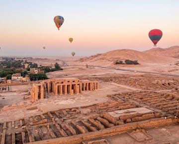 Hot air balloons float above ancient temple ruins and desert terrain in Luxor at sunrise, offering panoramic views of the Valley of the Kings region.