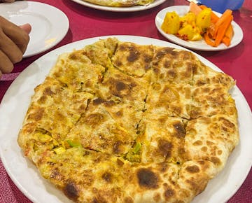 A hearty Egyptian stuffed bread dish cut into slices and served with a side of spicy pickled vegetables on a red tablecloth.
