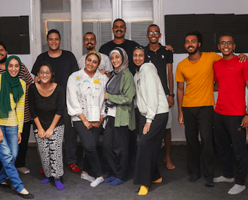 A group of smiling young adults pose together indoors, representing a diverse and empowered team participating in the women’s empowerment initiative.