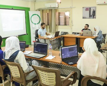 A group of women attend a computer-based workshop in a digital media lab, learning video editing and content creation.