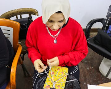 A young woman in a red sweatshirt practices threading and stitching fabric during a hands-on sewing session at the women’s empowerment center.