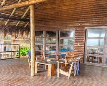 A shaded balcony with wooden chairs and a table provides a communal space for volunteers to relax outside their accommodation in Mozambique.