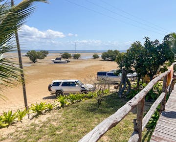 Vehicles parked on the sandy shoreline beside the IVHQ volunteer accommodation in Mozambique, with direct access to the tidal flats and ocean.