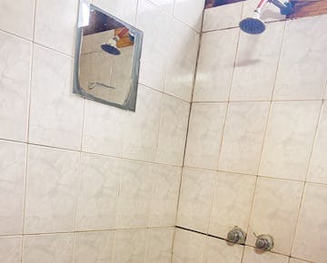 A tiled wall with showerhead and a small mirror in the shared bathroom facilities for volunteers staying in Mozambique.