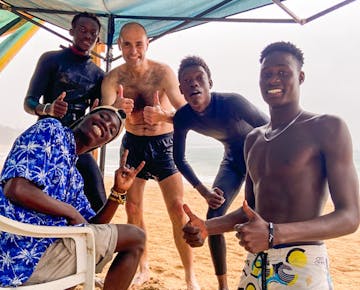 A group of volunteers and local surf instructors give thumbs-up on the beach in Mozambique, enjoying camaraderie and cross-cultural exchange.