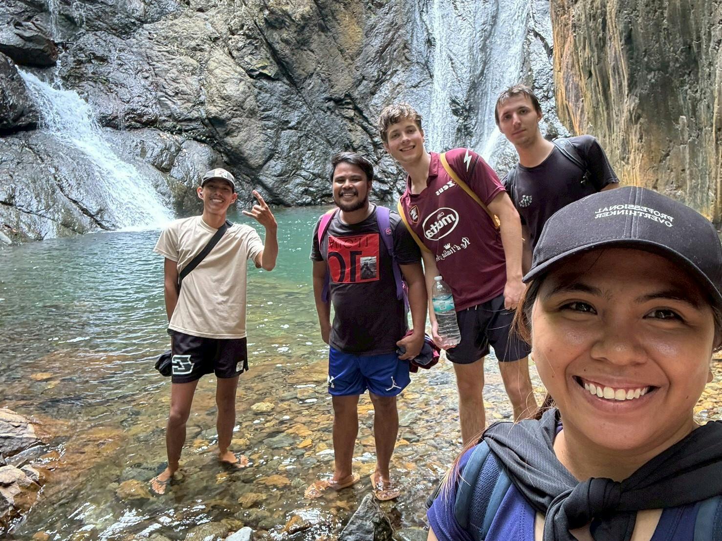 A group of volunteers stand for a photo at the base of a waterfall.