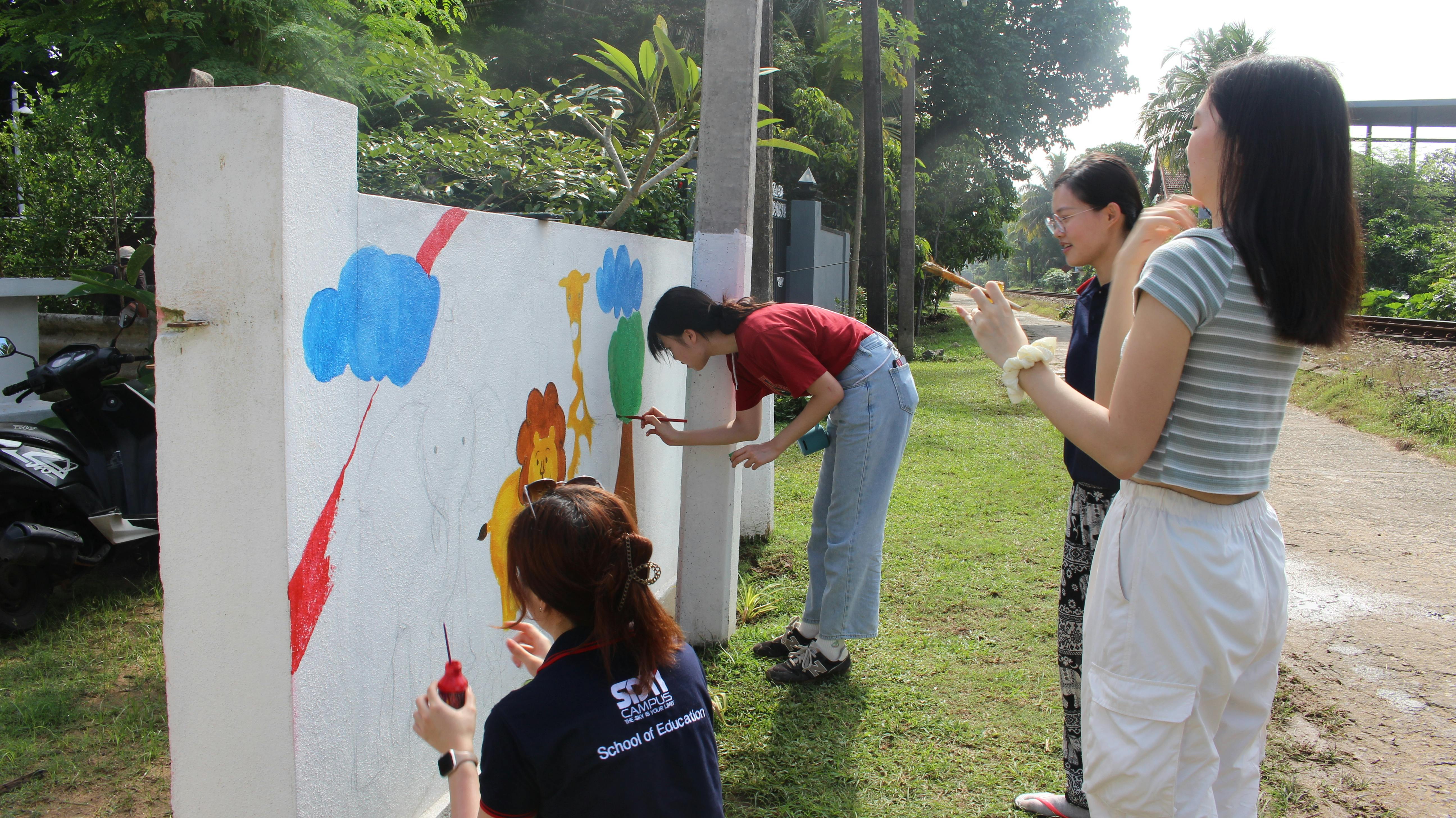 A group of IVHQ creative volunteers beautifying the daycare's outside wall to provide an engaging space for young children to come learn
