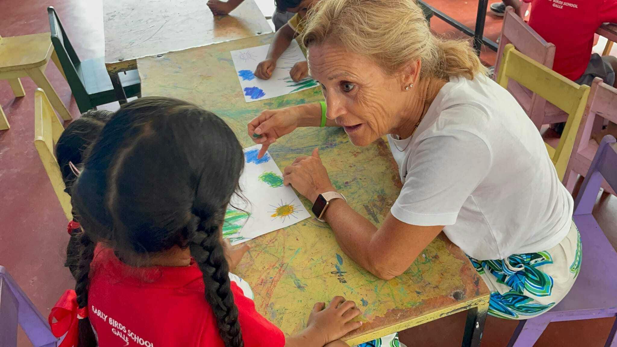 A senior IVHQ volunteer teaching a young student colors in English