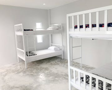 A bright bedroom with two white metal bunk beds, white bedding, and a concrete floor in a minimalist style.