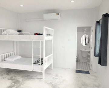 A tidy room with a white bunk bed, air conditioner, and a private bathroom visible through an open door.
