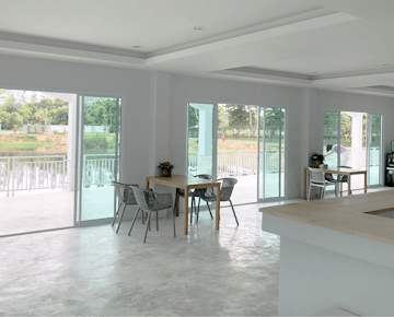 Dining tables and chairs next to large windows with views of trees and water, in a bright communal room.