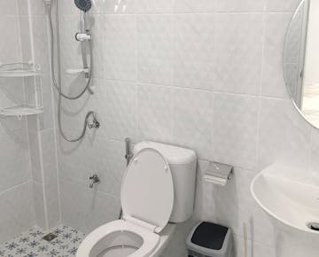 A clean, modern bathroom with a walk-in shower, toilet, and sink, featuring white tiles and a round mirror.