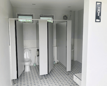 A clean bathroom with tiled floors, featuring toilet stalls with white doors and a urinal, in a modern accommodation facility.