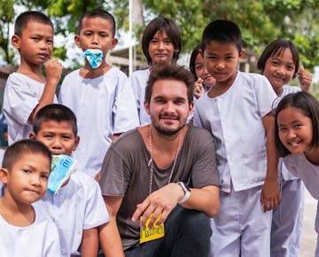 A volunteer crouches and smiles for a group photo with happy students wearing white uniforms outdoors.