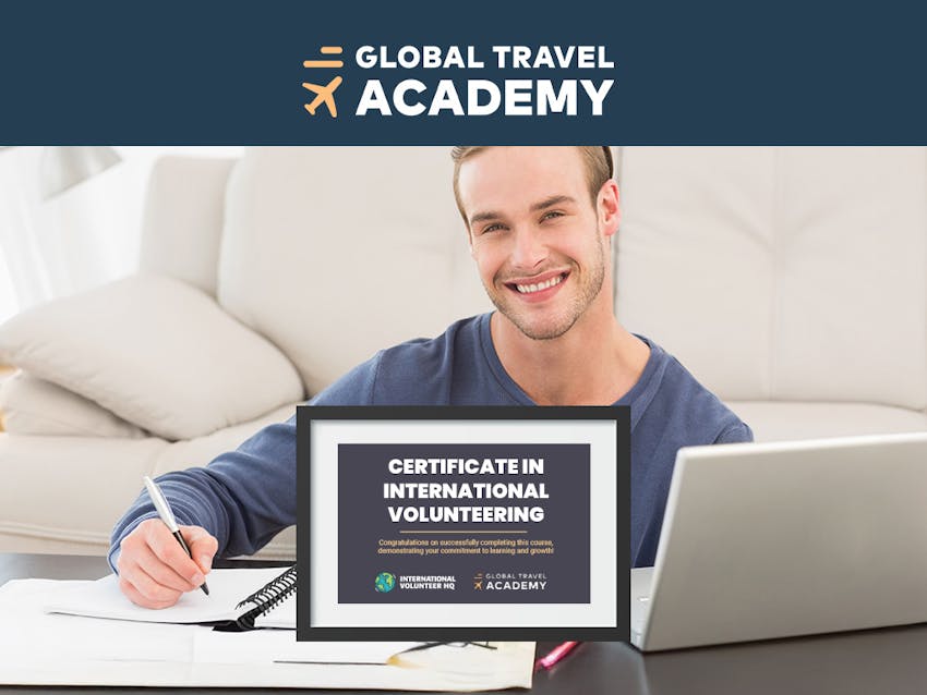 A man sits at a table and writes notes while studying for the International Volunteering course.