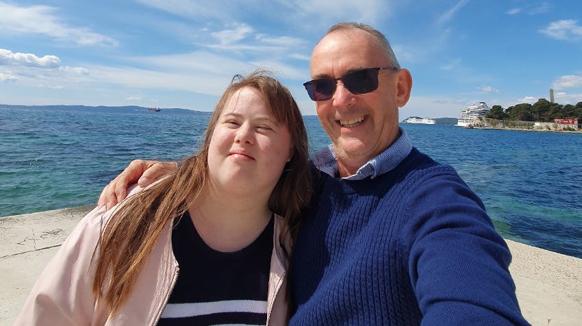 A smiling older male travel volunteer with sunglasses and a young woman enjoying a sunny day by the ocean in Croatia.