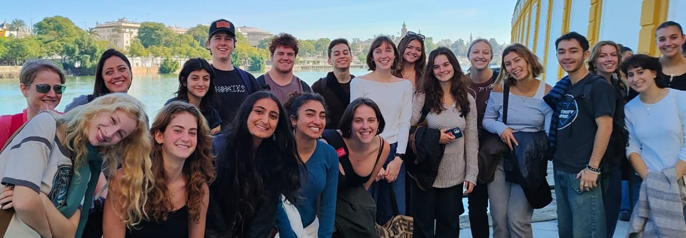 A group of smiling women and children stand together in colorful attire, conveying joy and community in front of a building with an open door.