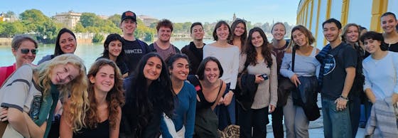 A group of smiling women and children stand together in colorful attire, conveying joy and community in front of a building with an open door.