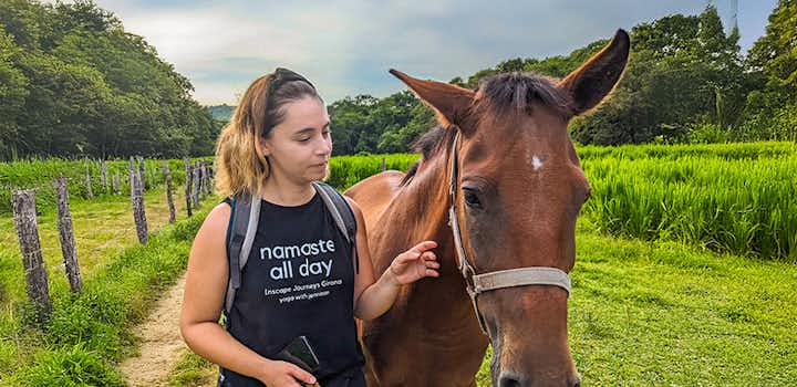 A female volunteer stands with a brown horse in a lush green field surrounded by trees in San José Manialtepec, Mexico.